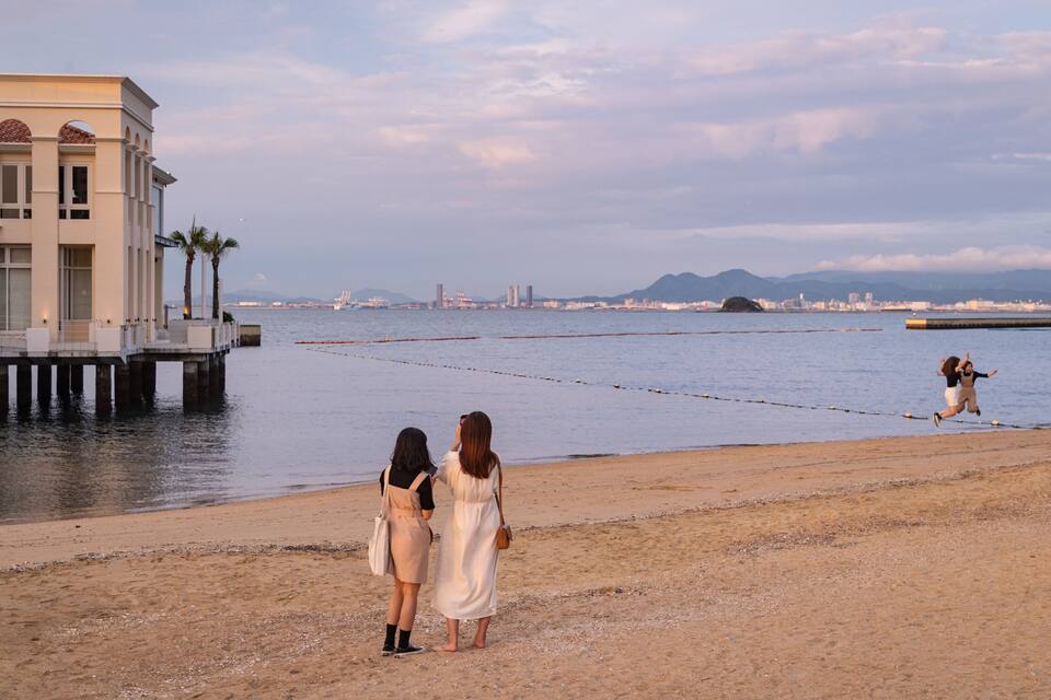 Uma praia com um cais e um horizonte urbano ao fundo.