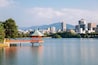 A lake with a gazebo, a city skyline, and mountains in the background.