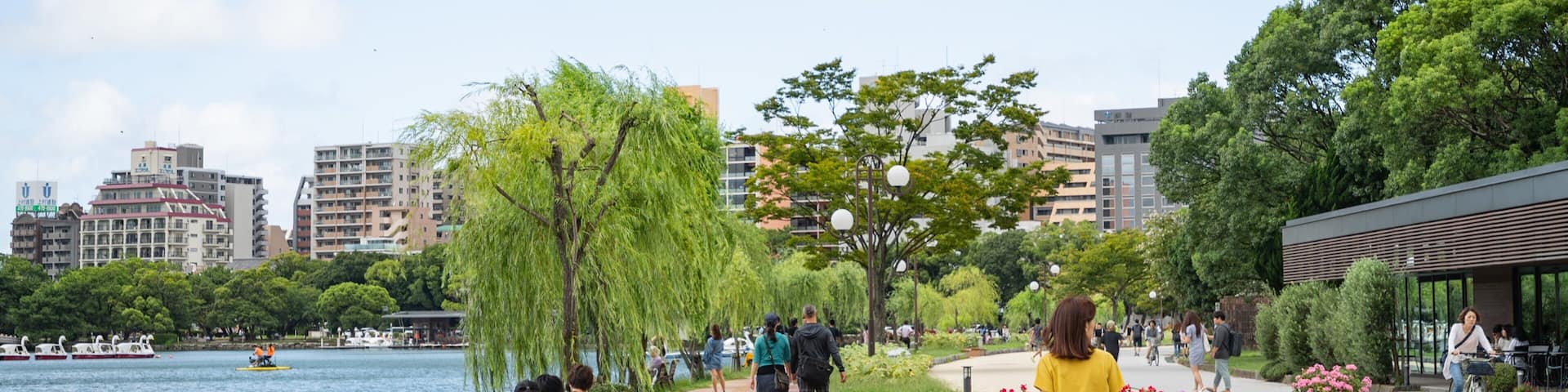 A riverside walkway with people walking, a dog, and boats on the water.