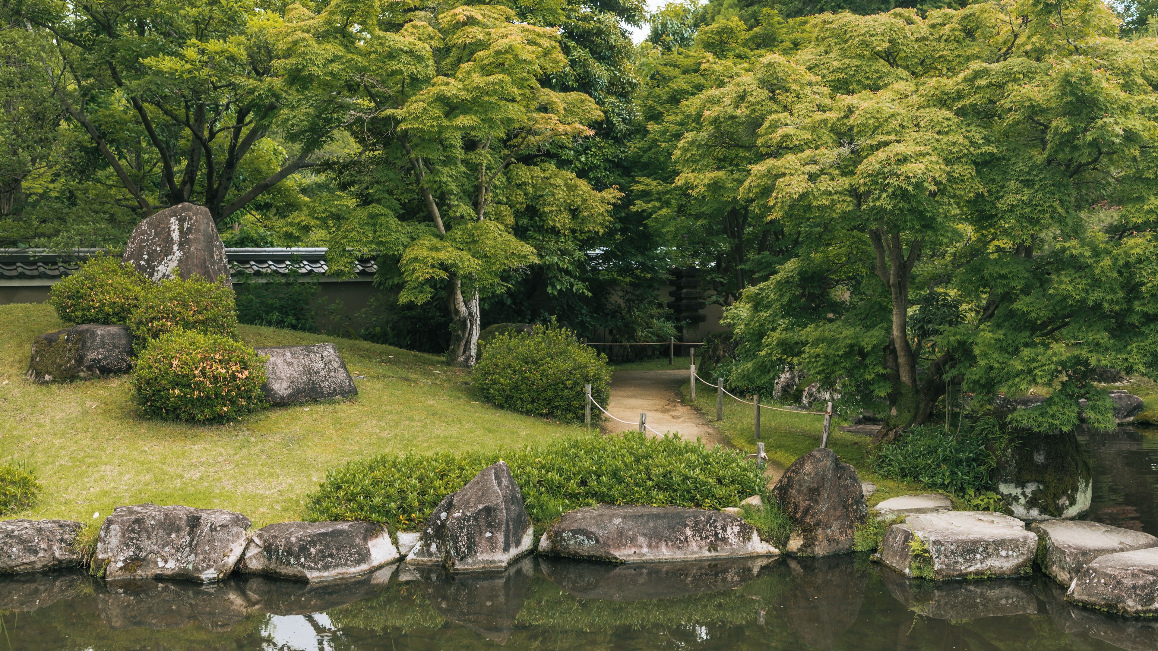 Un jardín sereno con un estanque, abundante vegetación y arquitectura japonesa tradicional.
