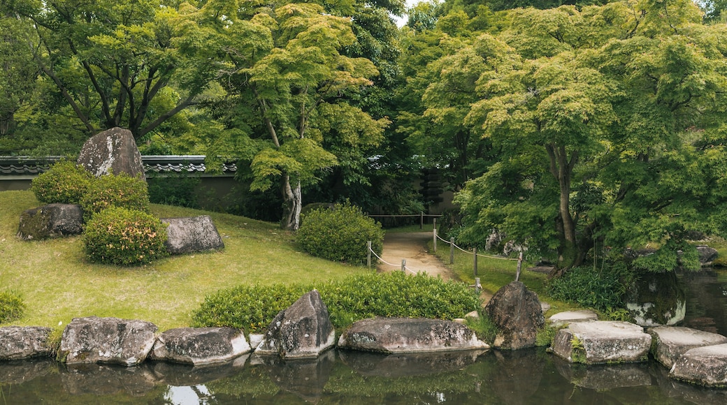 Un jardín sereno con un estanque, abundante vegetación y arquitectura japonesa tradicional.