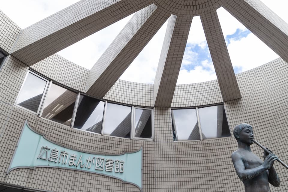 A modern building with a unique geometric design, featuring a large central structure and a statue of a person playing a flute.