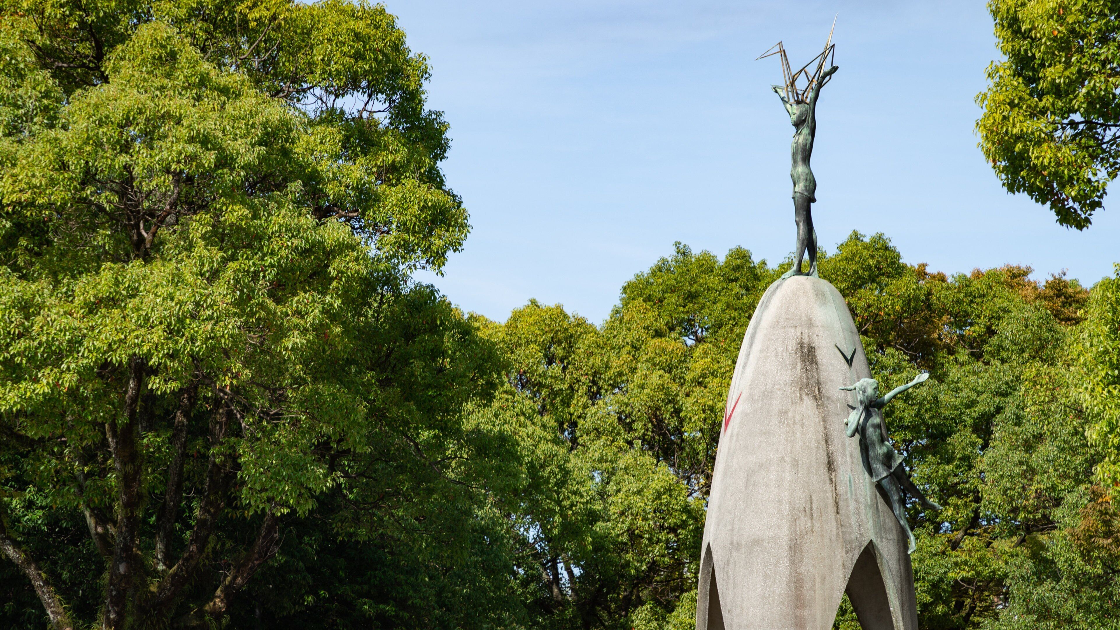A large stone statue of a figure with a bird on its head, surrounded by lush green trees.