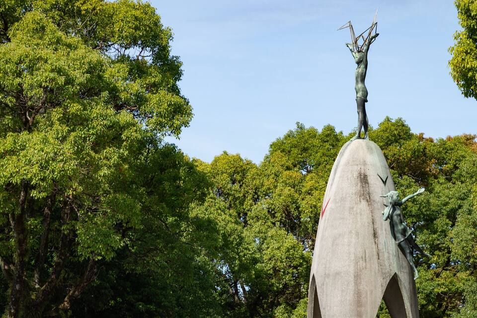 A large stone statue of a figure with a bird on its head, surrounded by lush green trees.