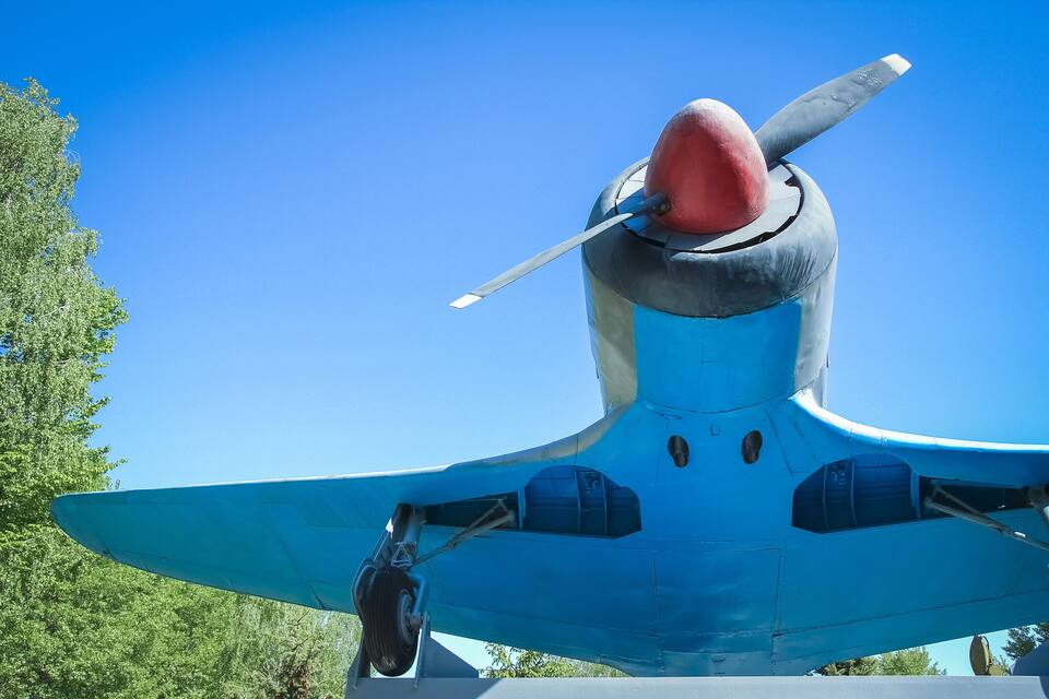 La cua d'un avió antic blau i vermell amb un hèlix, amb un cel blau clar de fons.