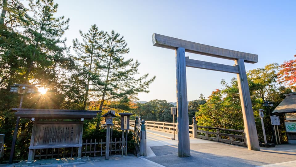 A traditional Japanese torii gate, a wooden structure with a horizontal beam, surrounded by trees and a clear sky.