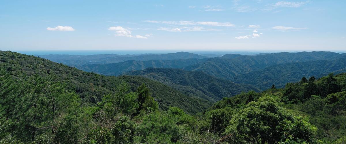 A mountainous landscape with dense green forests and a clear blue sky.