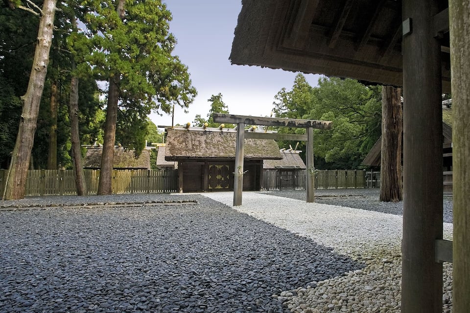 A traditional Japanese building with a thatched roof, surrounded by gravel paths and wooden fences.
