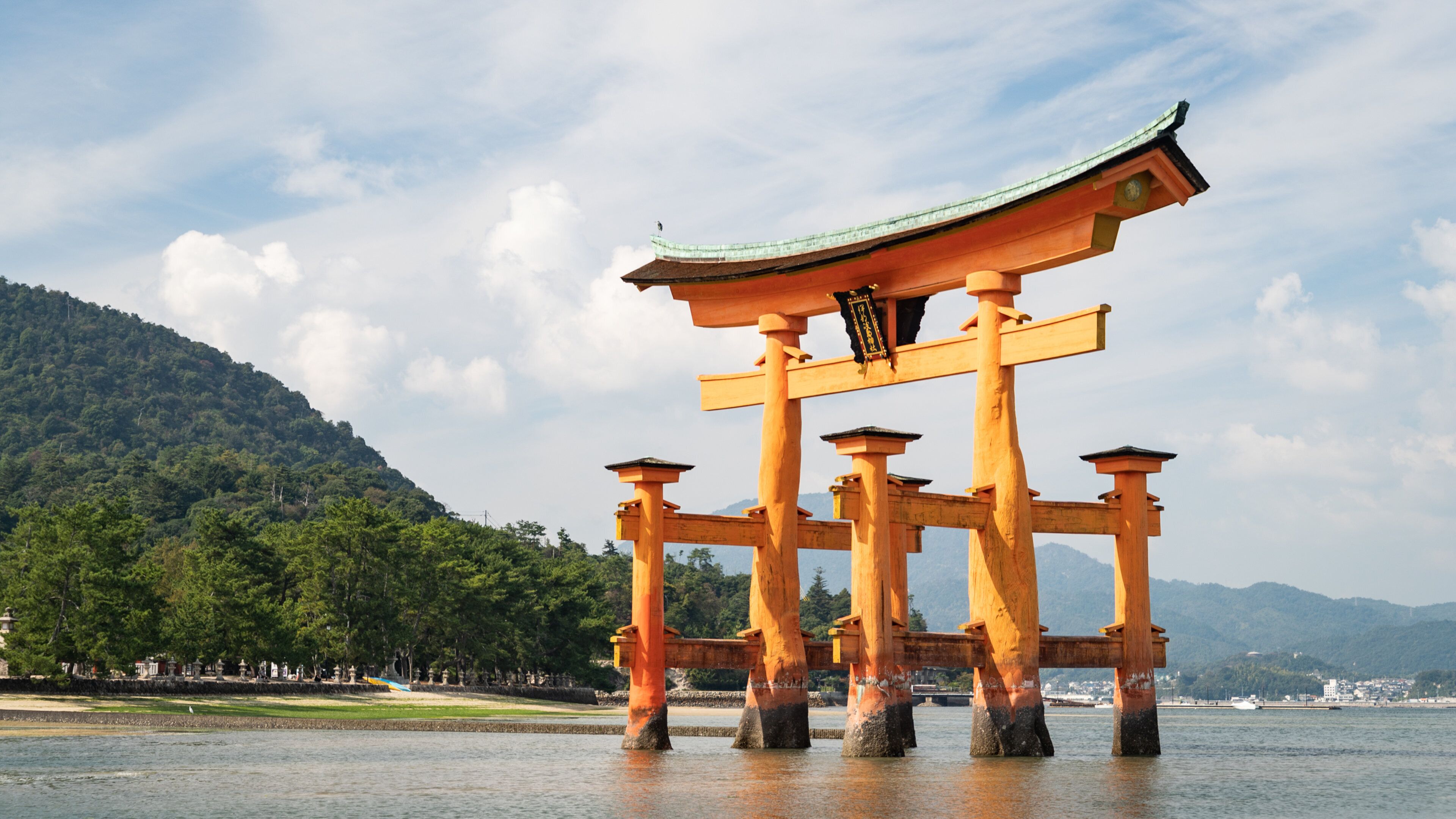A traditional Japanese torii gate with a curved roof, standing in a body of water with a mountainous backdrop.