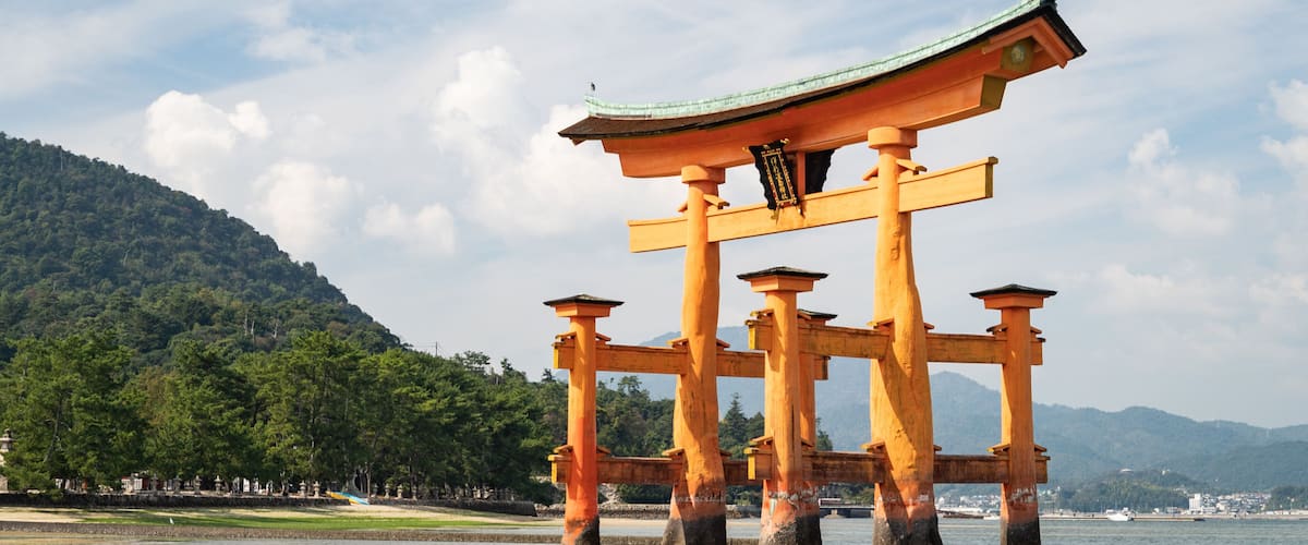 A traditional Japanese torii gate with a curved roof, standing in a body of water with a mountainous backdrop.