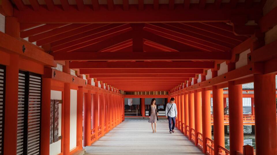 A corridor with red pillars and a wooden floor.