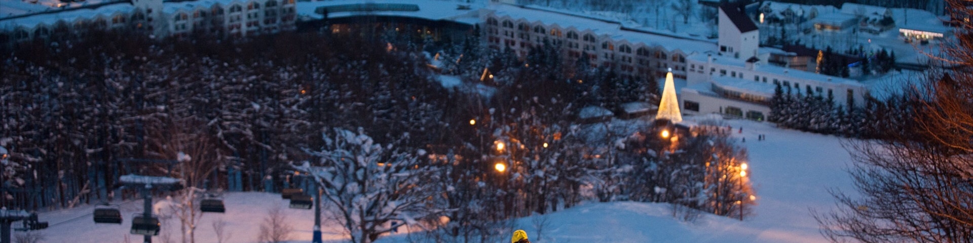 A snowy ski slope with a skier in motion, surrounded by snow-covered trees and buildings in the background.