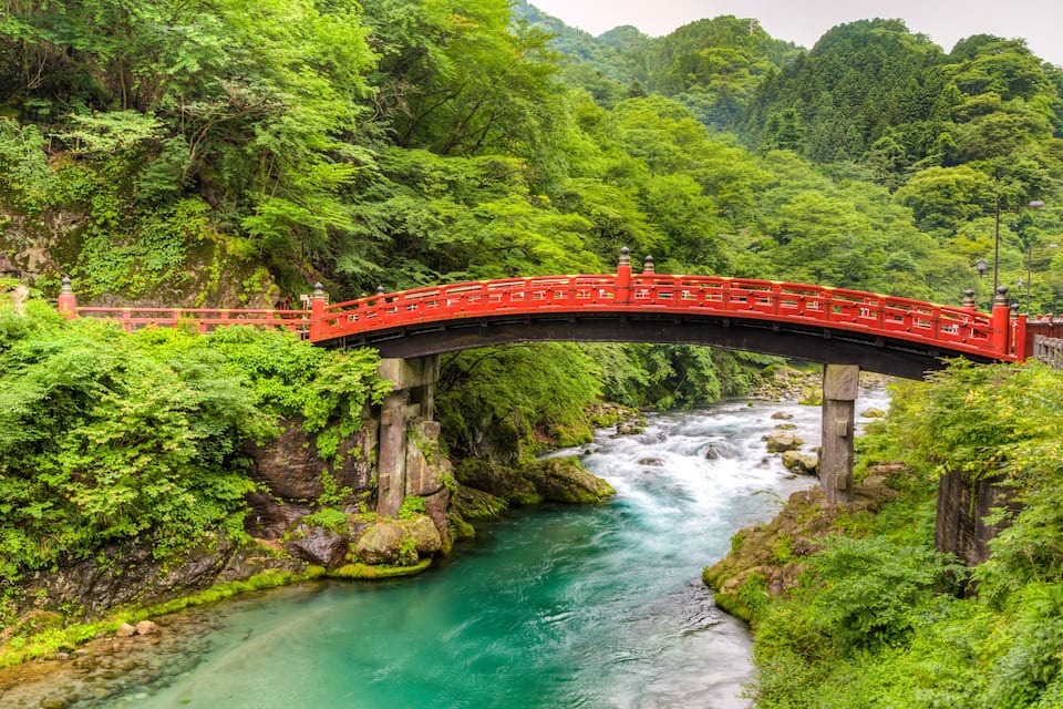 A red bridge over a turquoise river surrounded by lush greenery.