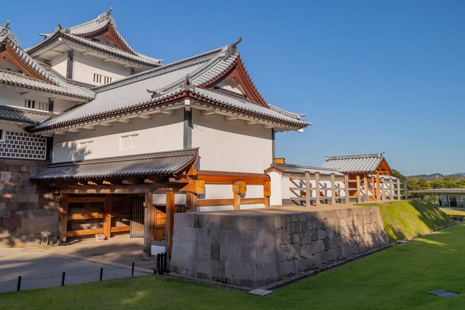 Um castelo japonês tradicional com vários telhados brancos e vermelhos, portões de madeira e uma parede de pedra.