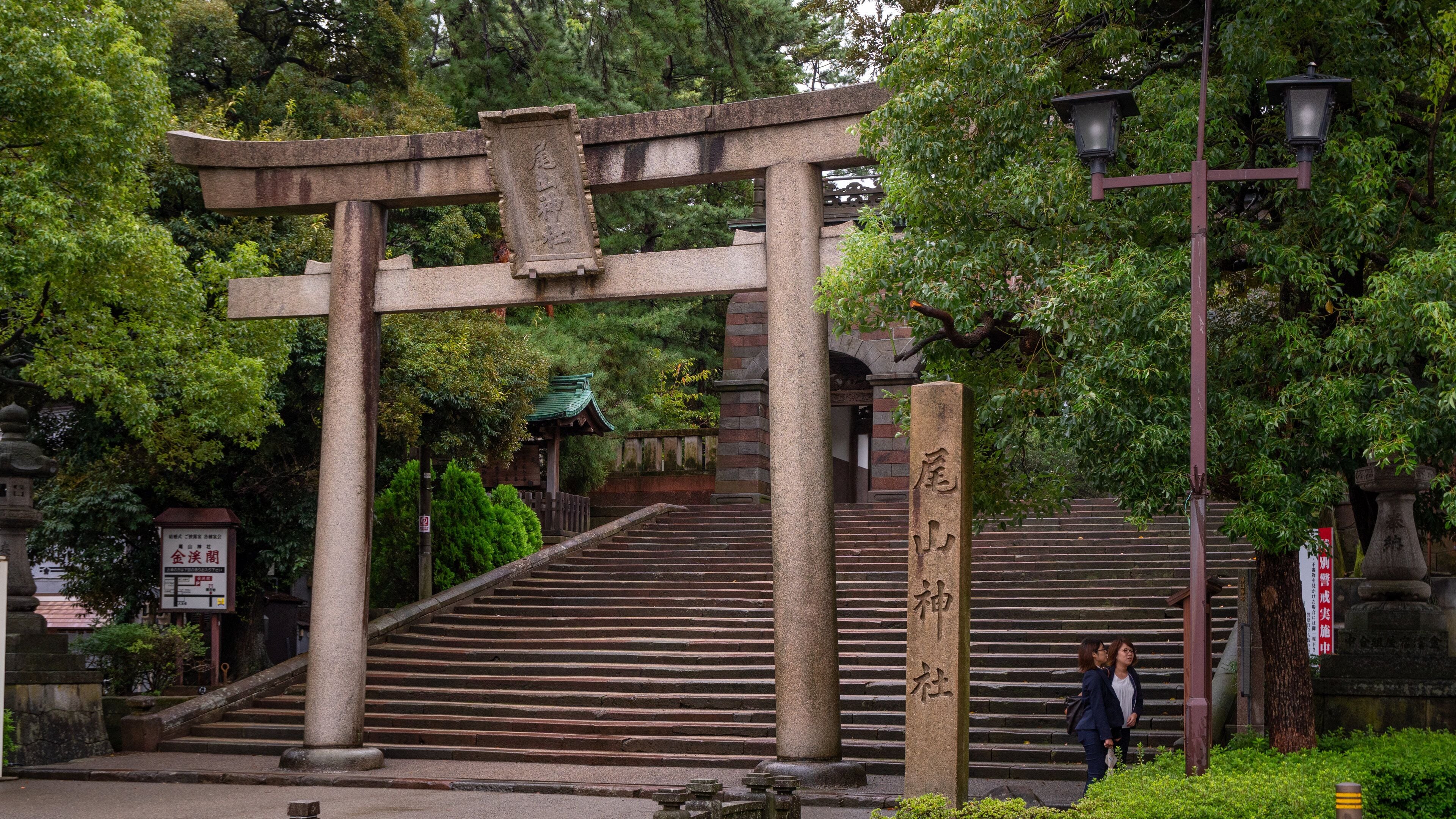 Un torii de piedra con escalones que conducen hacia él, rodeado de abundante vegetación.