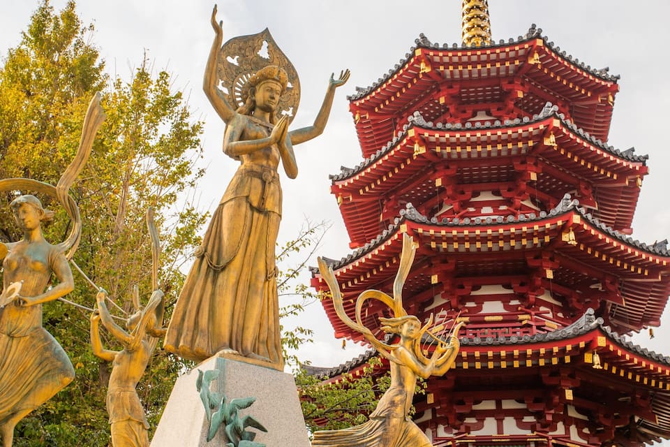 A traditional pagoda with red and gold accents, surrounded by statues of deities.