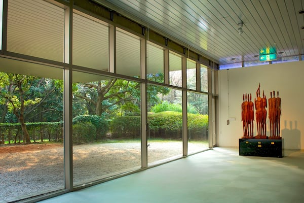 Une galerie spacieuse avec de grandes fenêtres, une sculpture représentant des figures humaines et un panneau de sortie vert.