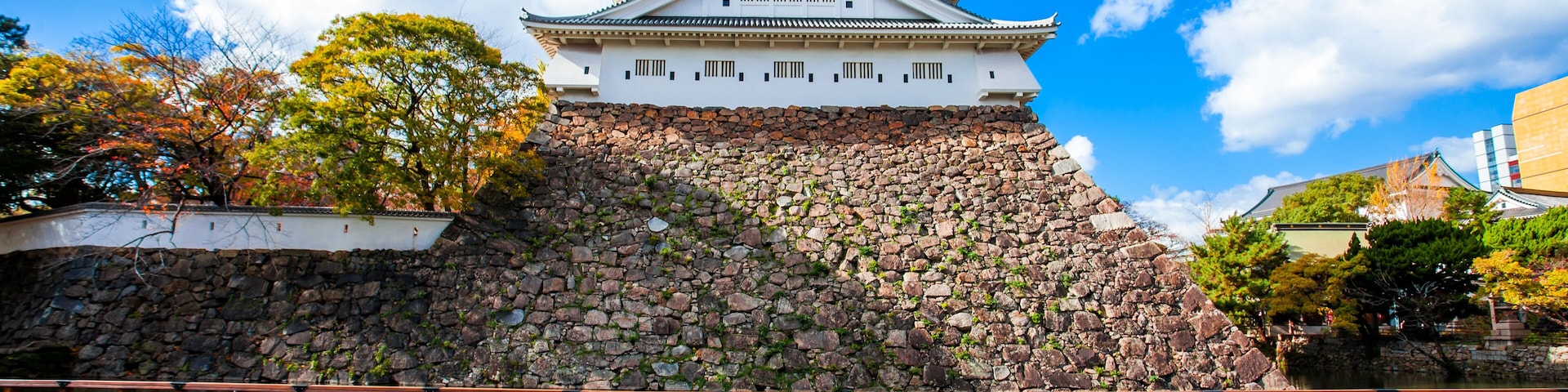 Un castillo japonés tradicional con varios niveles, una base de piedra y un cielo azul despejado con nubes.