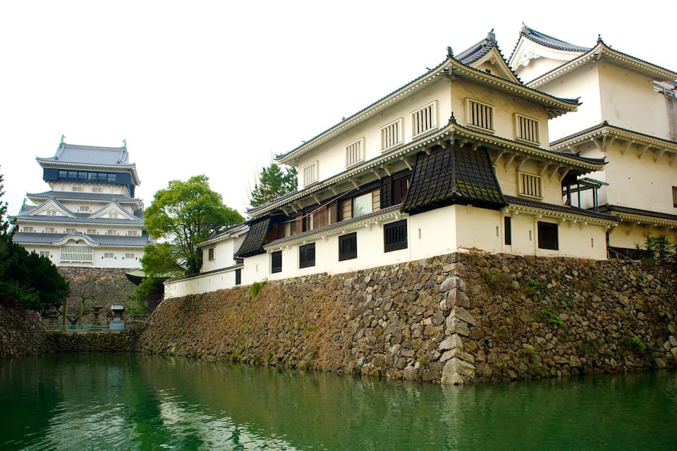 Un castell japonès tradicional amb una paret de pedra i un riu al primer pla.