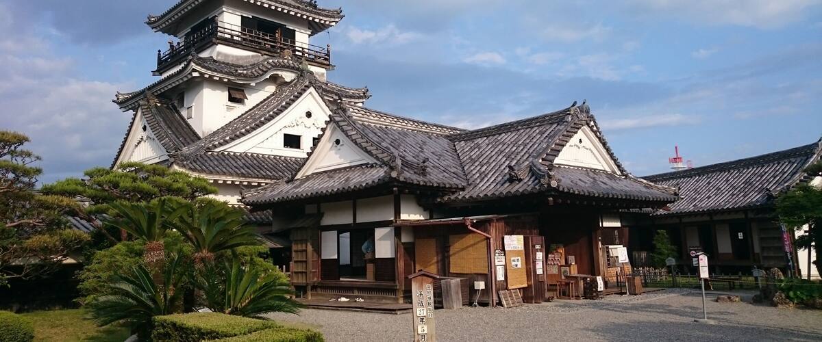 A traditional Japanese building with a prominent pagoda, surrounded by well-maintained gardens and a clear sky.