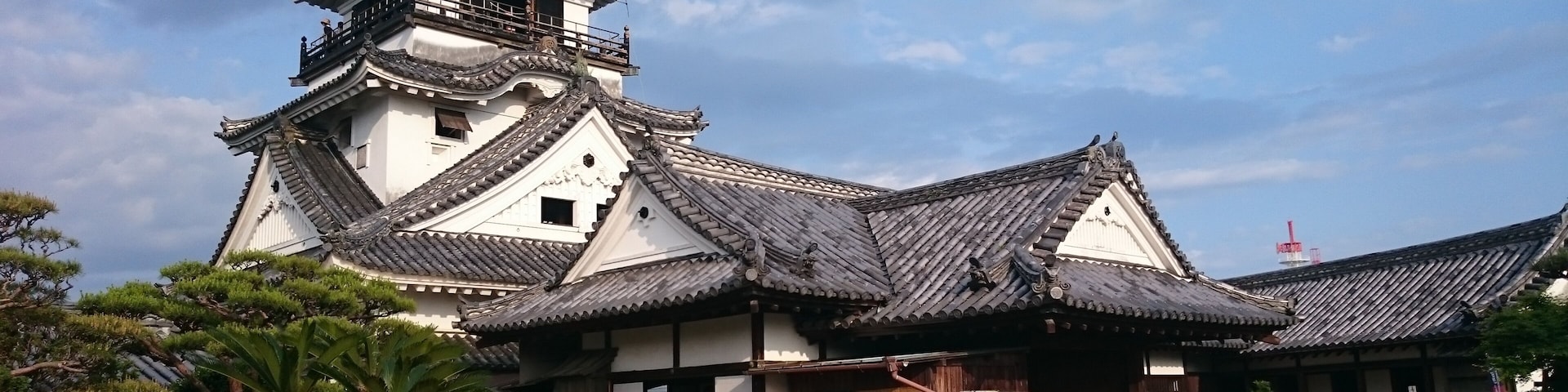 A traditional Japanese building with a prominent pagoda, surrounded by well-maintained gardens and a clear sky.