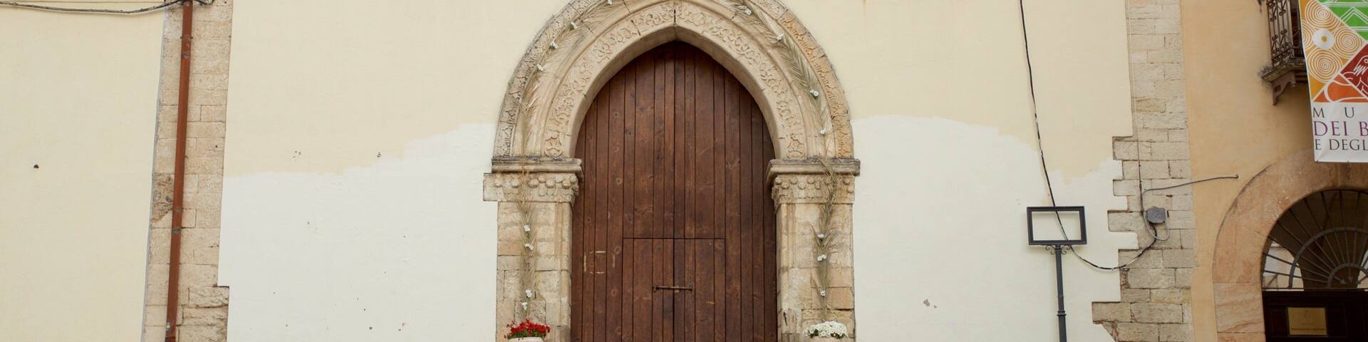 Entrada de una iglesia con una puerta de madera grande, escalones de piedra y un campanario.
