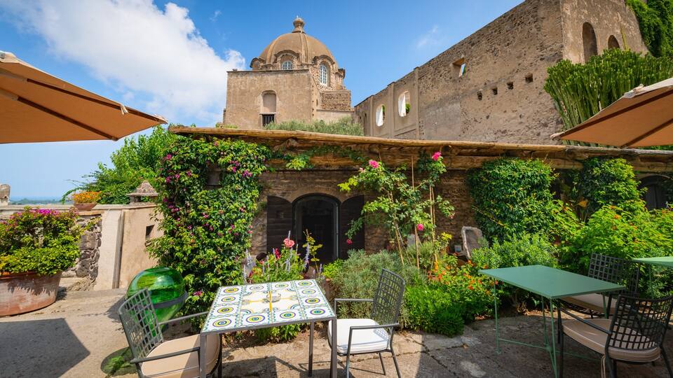 A courtyard with a table and chairs, surrounded by lush greenery and a historic building with a dome.