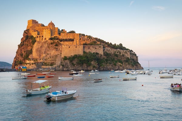Una cittadina costiera con un castello storico a picco sul mare, circondata da imbarcazioni nel porto.