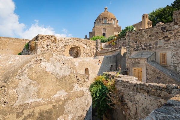 Un edificio storico in pietra con una cupola, circondato da rovine antiche e vegetazione.