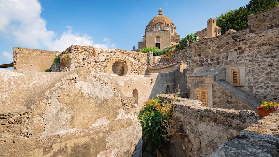A historic stone building with a dome, surrounded by ancient ruins and greenery.