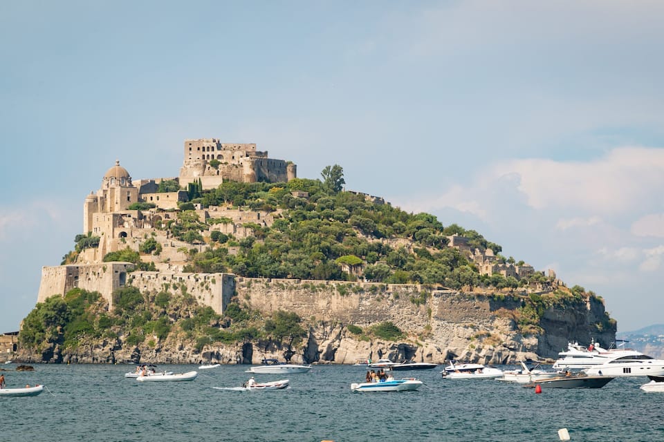 Un site historique fortifié, perché sur une colline, avec un château, entouré d’eau et de bateaux.