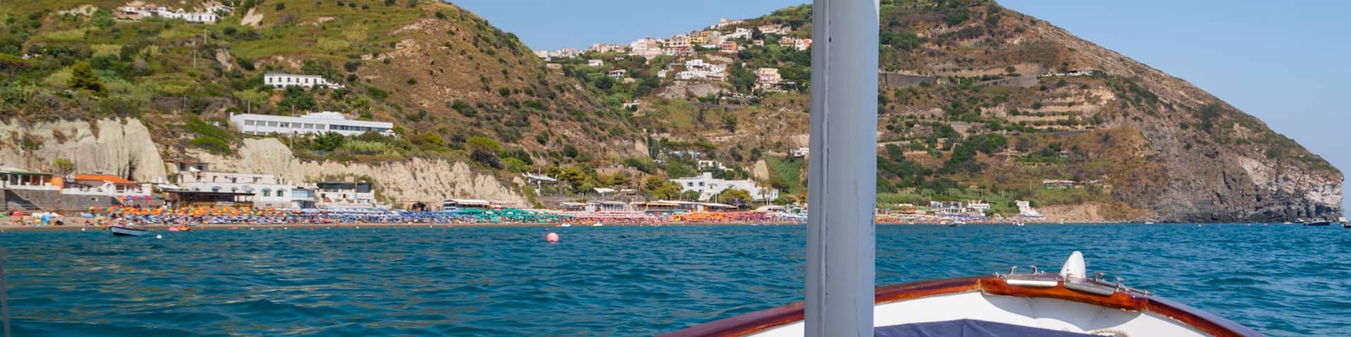 A boat on calm sea waters with a coastal town and hills in the background.