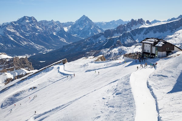 Ein schneebedeckter Berghang mit Skifahrern und einer Berghütte.