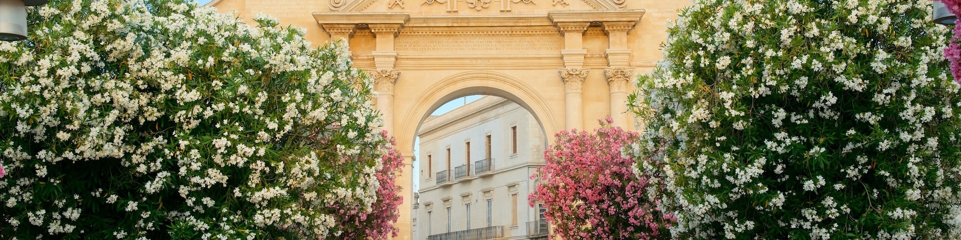 Un arco histórico con detalles tallados y un edificio al fondo.