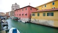 A canal with boats docked, colorful buildings, and a bridge in the background.