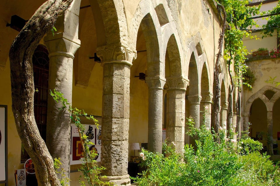 An ancient stone building with arches and columns, surrounded by greenery and a clock.