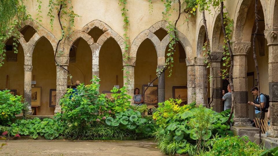 Un patio histórico con arcos de piedra, abundante vegetación y obras de arte enmarcadas.