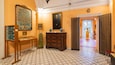 A hallway with patterned floor tiles, a large framed painting, a wooden cabinet, and a door with a decorative grille.