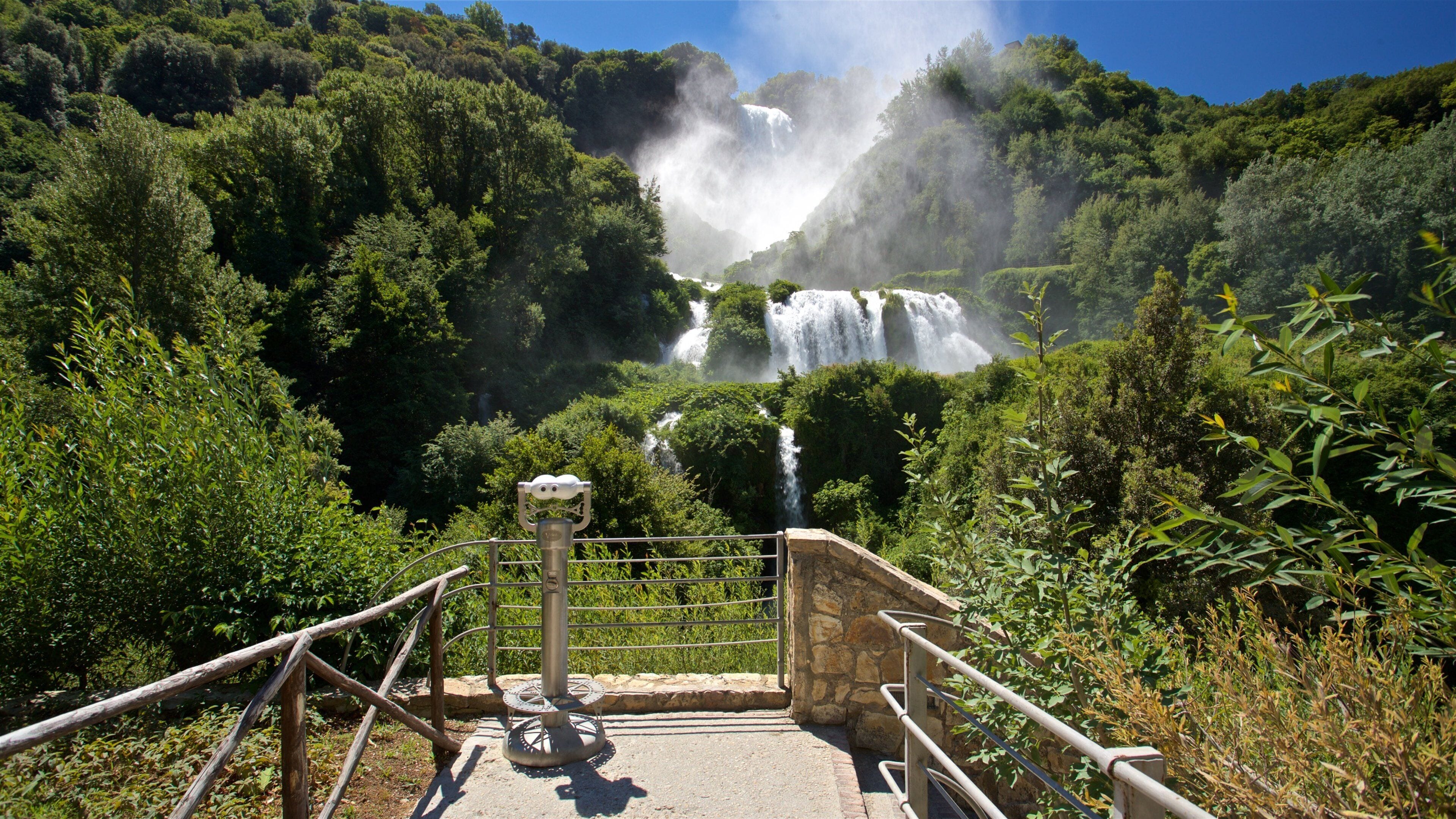 Une cascade entourée d’une végétation luxuriante et une plateforme d’observation en pierre.