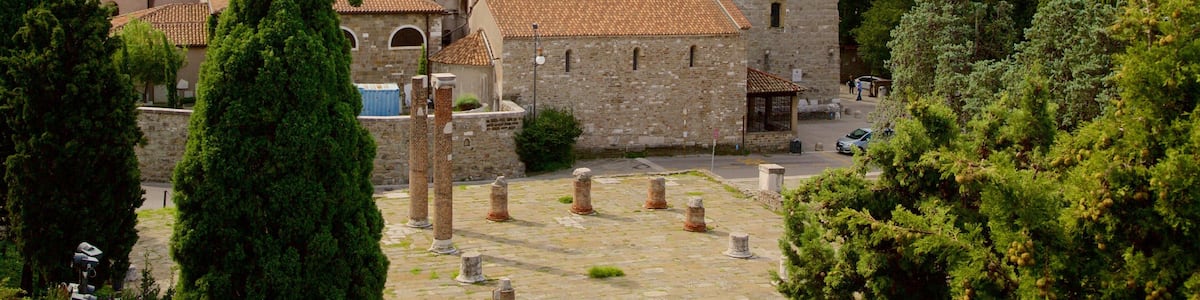 A historic stone building with a bell tower, surrounded by trees and a paved courtyard.