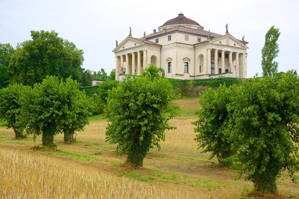 A historic building with a dome and columns, surrounded by a field of crops and trees.