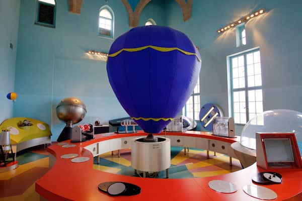 A colorful room with a large blue hot air balloon, a yellow spherical object, and a red table with various items.