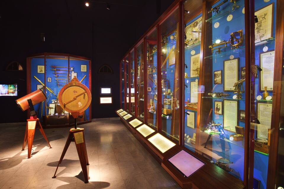 Una mostra de museu amb instruments científics històrics, incloent un telescopi gran i un rellotge.