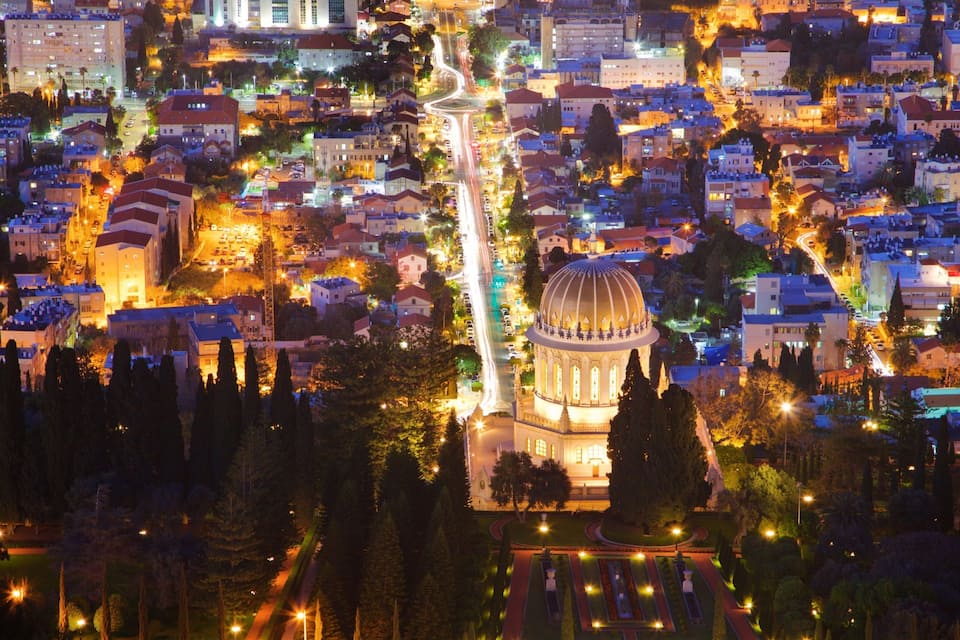 A cityscape at night with a prominent dome-shaped building in the center, surrounded by illuminated streets and residential buildings.