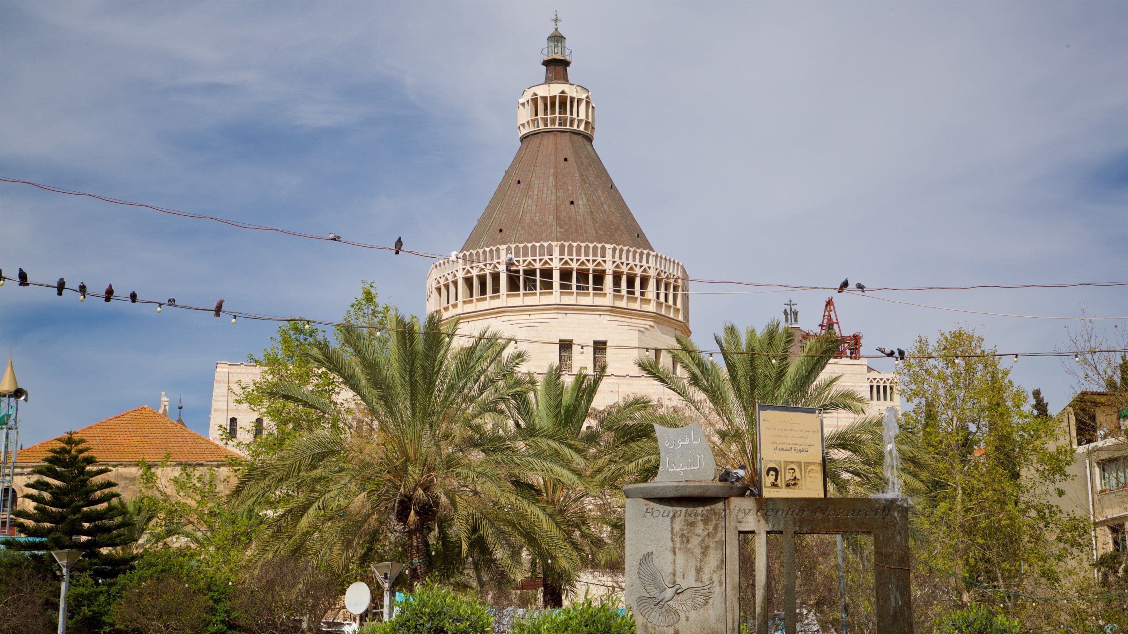 A historic building with a dome and minaret, surrounded by palm trees and a street lamp.
