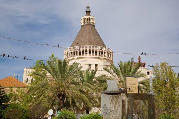 Un bâtiment historique doté d’un dôme et d’un minaret, entouré de palmiers et illuminé par un lampadaire.