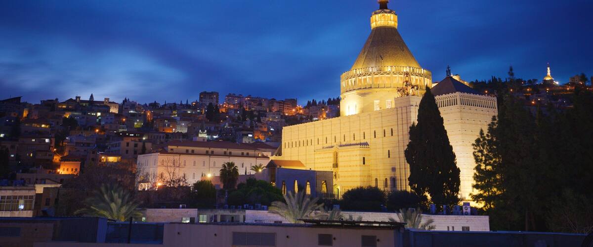 A historic building with a prominent dome and a tower, surrounded by a cityscape at dusk.