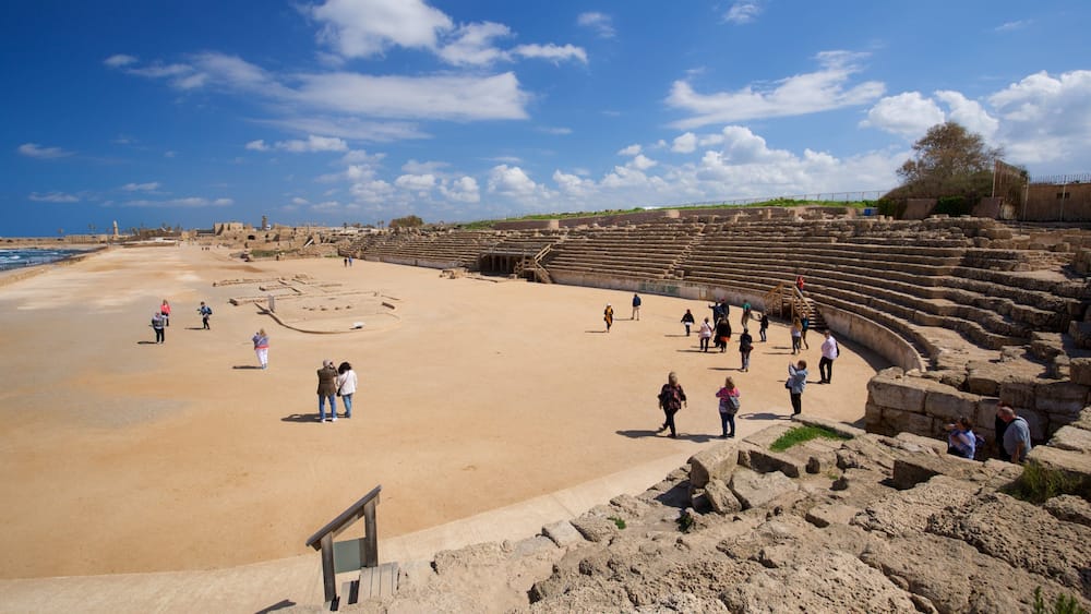 An ancient amphitheater with ruins and a sandy beach.