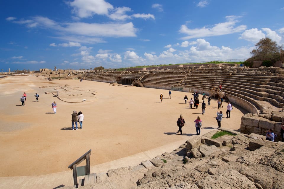 Een oud amfitheater met ruïnes en een zandstrand.
