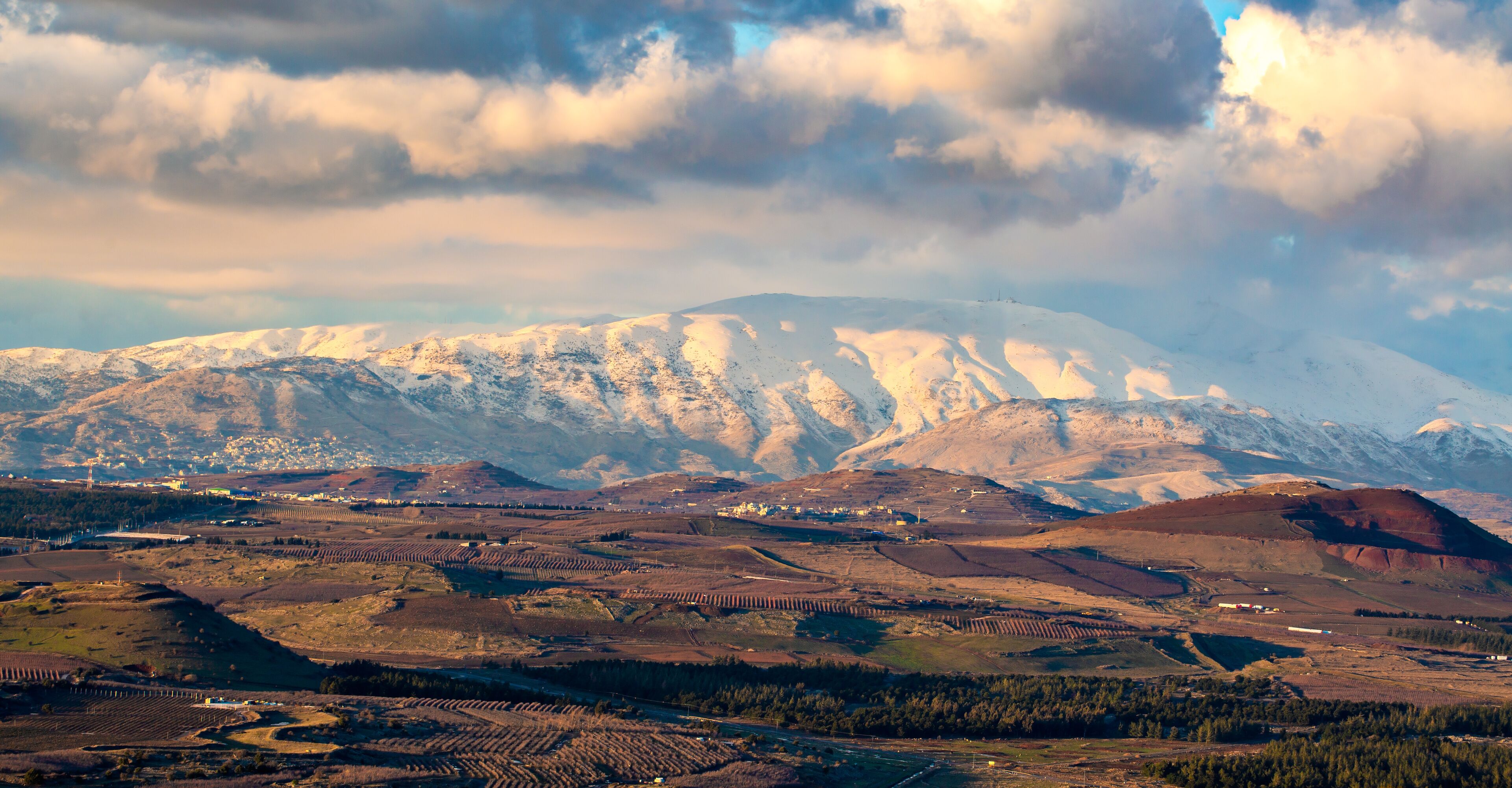 A snow-capped mountain range with terraced fields and a cloudy sky.